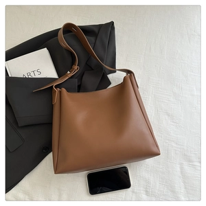 Detailed macro view of caramel leather tote bag on textured white fabric with a blazer