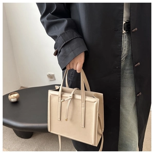 Chic beige tote bag styled with a black trench coat and casual denim jeans