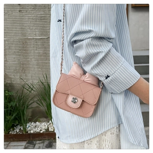 Detail of pink quilted crossbody bag featuring a leather bow and flower metal clasp