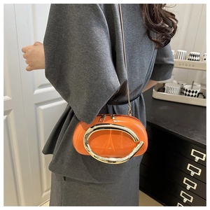 Detail of bright orange glossy clutch bag featuring a large gold C-shaped metal ornament