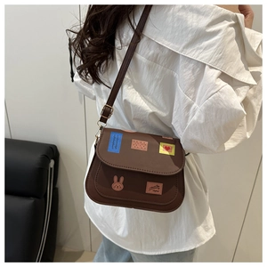 Détail d'un sac bandoulière marron avec écussons colorés porté par un mannequin