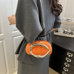 Glossy orange leather crossbody bag with bold gold metal handle and chain strap on model