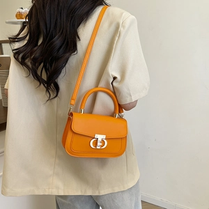 Chic orange leather shoulder bag with metal logo clasp worn with a beige blazer jacket