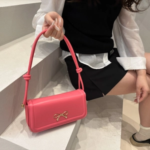 Pink crossbody bag with a metal bow accent and decorative knot handle on grey stairs