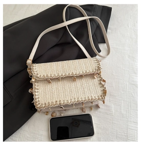 Detail of woven straw crossbody bag with shell pendants and bohemian fringe accents