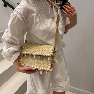 Woven straw crossbody bag with shell fringe and beads on a stylish white dress