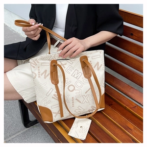 Detail view of cream tote bag with brown straps and mini coin purse charm on a bench