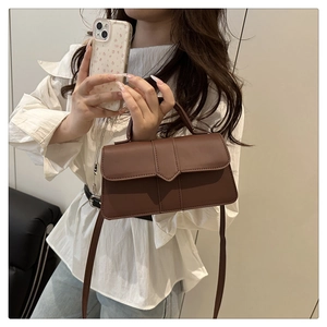 Dark brown square crossbody bag with hand strap and V-shaped flap detail shown by model