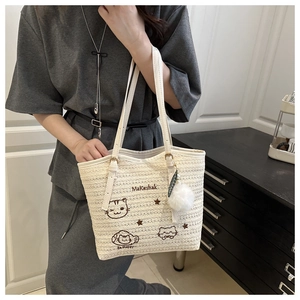 Détail d'un sac cabas tissé avec broderie de chat et breloque pompon blanc doux
