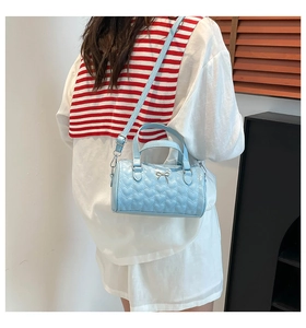 Sac cylindrique bleu clair à surpiqûres cœur porté avec bandoulière par un mannequin