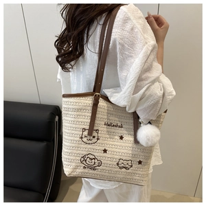 Détail du sac cabas tissé avec broderie de dessins animés et pendentif pompon en peluche