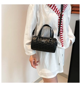 Détail du sac Boston noir à surpiqûres cœurs, avec nœud argenté et bandoulière