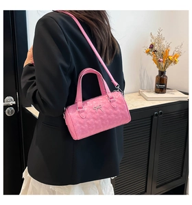 Détail du sac cylindrique rose à surpiqûres cœurs avec nœud argenté et bandoulière