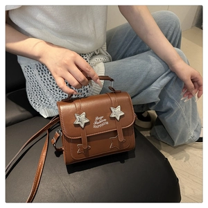 Close-up of brown crossbody bag with silver star studs and embossed fashion typography