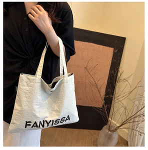 Detail of canvas tote bag with letter print, magnetic metal button and branded side label