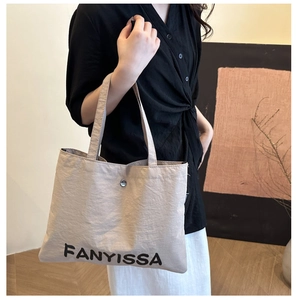 Close-up of beige canvas tote bag with black FANYISSA lettering and metal button detail