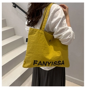 Detail of a bright yellow canvas tote bag with black FANYISSA lettering and shoulder strap