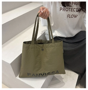 Detail of dark green nylon tote bag featuring metal clasp and printed logo on textured fabric