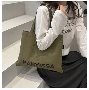 Olive green canvas tote bag with black letter print worn by model on stairs