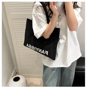 Detail of a casual black canvas tote bag with white FANYISSA lettering worn by a model