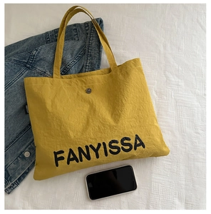 Detailed close-up of yellow canvas tote bag with black letter print and metal snap button