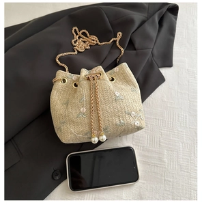 Detail of straw bucket bag with floral embroidery, chain strap and pearl drawstrings