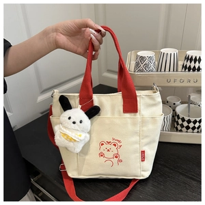 Detail of canvas tote bag with red handles, cartoon bear print and plush bunny charm