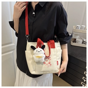 Détail du sac cabas en toile avec bandoulière rouge et charm lapin porté par un mannequin