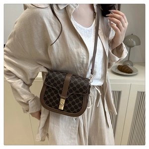 Close-up of vintage brown saddle bag with monogram pattern and gold buckle detail