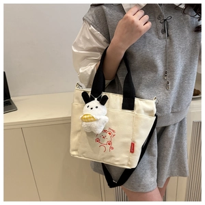 Detail of canvas tote bag with red cartoon illustration and white plush pendant accessory