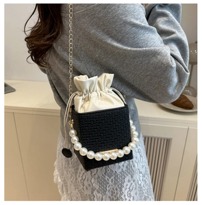 Close-up of woven bucket bag featuring pearl handle and gold chain strap detail