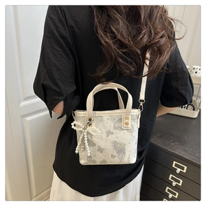 Détail du sac seau en tissu crème avec imprimé papillon et accessoire nœud en perles