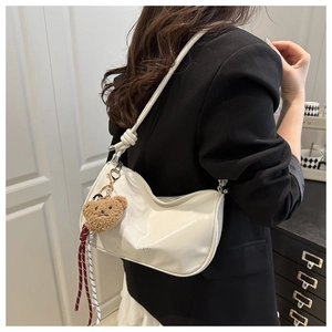 Detail of cream glossy leather pillow bag with brown plush bear charm and fashion logo