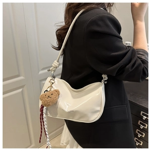 Chic cream pillow bag with glossy finish and cute bear charm worn by model in black blazer