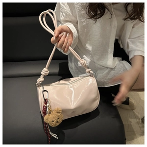 Detail of glossy beige pillow bag featuring handcrafted knot strap and plush bear charm