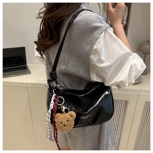 Detail of black patent leather shoulder bag with plush bear charm and ribbon accent