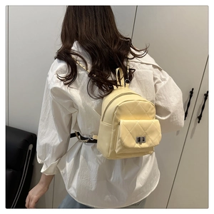 Detail of yellow quilted mini backpack with silver metal twist lock worn by a model