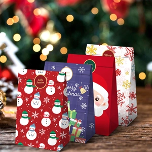 Set of four festive Christmas paper gift bags with Santa and snowman prints on wood surface
