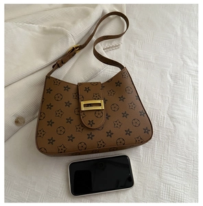Top view of a brown patterned underarm bag next to a smartphone for size reference