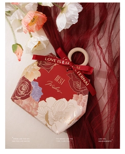 Close-up of red envelope wedding favor box with wooden ring handle and floral gold print