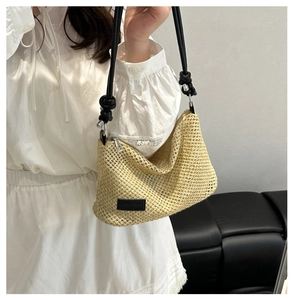 Close-up of beige woven straw crossbody bag with knotted black leather strap detail