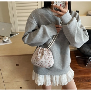 Close-up of floral drawstring crossbody bag worn over a grey casual sweatshirt