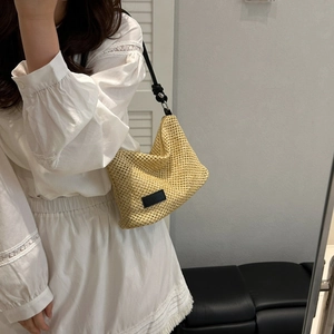 Minimalist beige woven straw tote bag with black leather shoulder straps and metal rings