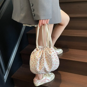 Floral drawstring handbag with red flower patterns held by a model on wooden stairs