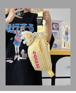 Gros plan du sac bandoulière en nylon jaune avec logo OOXBAG et breloque peluche