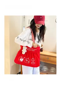 Detail of red canvas tote bag with apple print, checkered strap and plush bear charm
