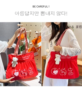 Detail of red canvas tote with apple prints, checkered straps and plush bear charm