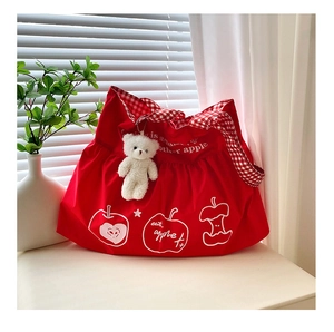 Detail of red canvas tote bag with apple print, gingham straps and plush bear charm