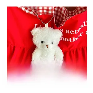 Close-up of cute white plush bear charm with metal chain on apple red tote bag