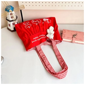 Detail of red nylon tote with apple print, red checkered lining and bear keychain